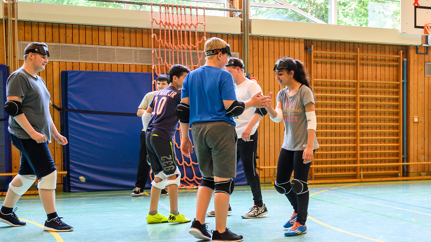 Schüler in der Sporthalemit Knie und Elenbogenschoner beim Goalballspielal